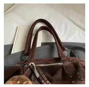 Détail du sac vintage marron avec clous, pendentif en peluche et poignée lisse