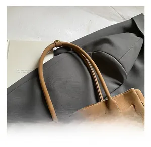 Close-up of brown suede tote bag with slim handles and metal buckle on grey blazer