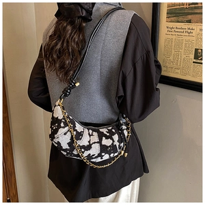 Detail of a cow print crescent shoulder bag with knotted leather strap and gold chain detail
