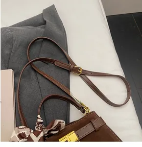 Detail of a brown suede crossbody bag with a decorative silk scarf on the handle