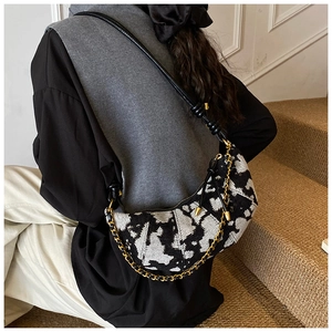 Detail of cow print croissant bag with gold chain strap and black leather shoulder strap