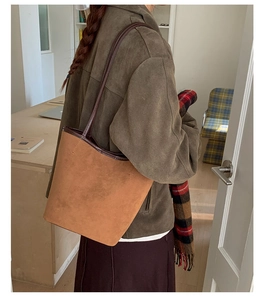 Detail of vintage brown suede tote bag with leather trim on model in cozy indoor setting