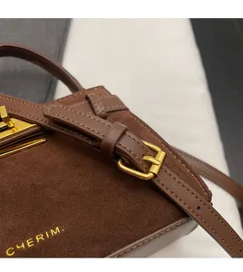 Detail of dark brown suede Kelly bag featuring gold buckles and leather shoulder strap