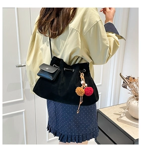 Detail of black suede bucket bag with silver eyelets, mini pouch, and colorful pom-poms