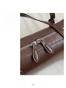 Detail of dark brown cylindrical bag showing premium dual zipper and leather texture