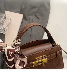Close-up of brown leather bag featuring golden twist lock and decorative silk scarf handle