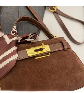 Detail of brown suede handbag with gold lock and decorative silk scarf on handle