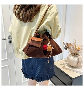 Detail of suede bucket bag with leather strap, mini pouch, and colorful pompom charms