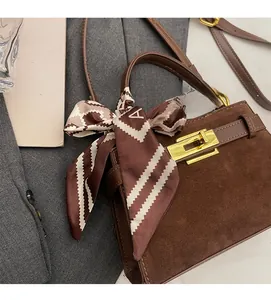 Close-up of brown suede handbag with golden turn-lock and elegant silk scarf detail