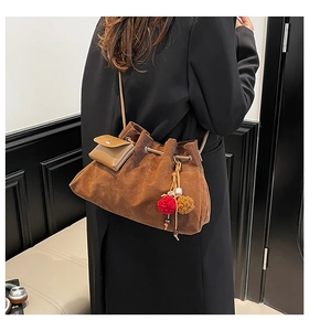 Detail of vintage brown suede bucket bag with drawstring closure and pompom charm accessory