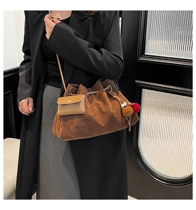 Detail of a brown suede bucket bag with decorative mini pouch and colorful pompom