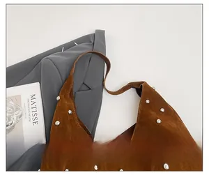 Close-up of brown suede shoulder bag featuring silver metal rivets and urban styling