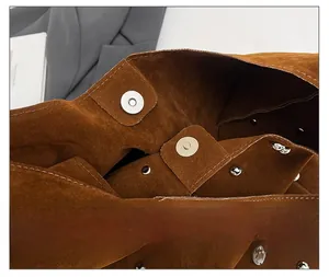 Detail of brown suede crossbody bag showing the magnetic closure and silver rivet decor
