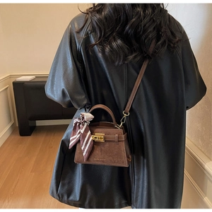 Macro shot of dark brown suede handbag with golden clasp and silk scarf detail