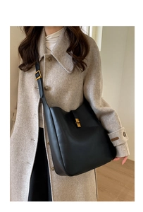 Detail of minimalist black matte leather hobo bag with golden buckle on a beige coat