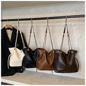 Detail view of large faux leather bucket bags in white, black, and brown with chain straps