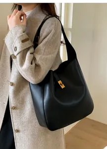 Detail of minimalist black leather hobo bag with gold turn-lock on a grey wool coat