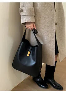 Detail of black leather bucket bag with gold metal buckle on female model in coat