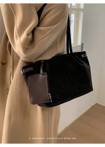 Chic black velvet tote bag with brown leather handles worn by a model in a camel coat