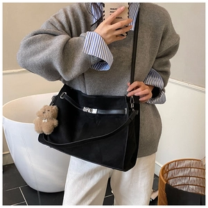 Detail of black suede tote bag featuring silver lock buckle and cute plush bear charm