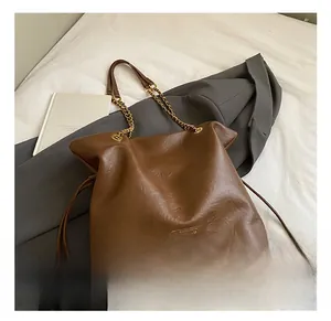 Detail of brown leather bucket bag with gold chain strap on grey blazer fabric