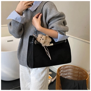 Detail of a black matte tote bag with slim metal strap and cute plush puppy charm