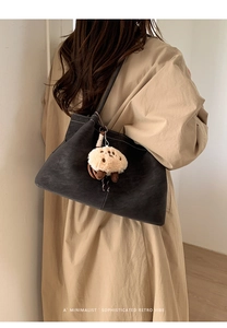 Detailed view of black suede tote bag with contrast stitching and plush puppy pendant