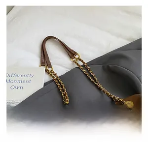 Detail of deep brown leather handle featuring a gold chain and elegant metal hardware