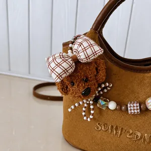 Details einer braunen Wildledertasche mit Plüschwelpen-Anhänger und Perlenkette