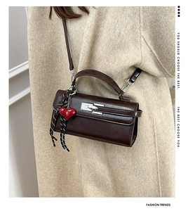 Détail d'un sac à main en cuir marron foncé avec fermoir argenté et pendentif coeur