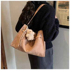 Brown large capacity suede tote bag with plush bear charm worn by a model in a cozy room