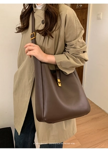 Detail of a brown leather bucket bag featuring a gold metal clasp and retro minimalist style