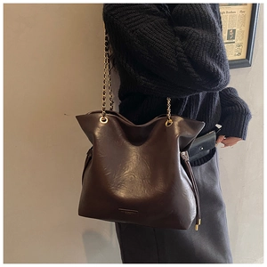 Lifestyle view of large dark brown bucket bag with gold chain strap on model shoulder
