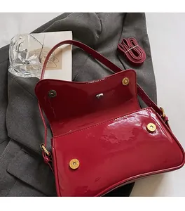 Detail of red patent leather shoulder bag showing the functional magnetic buckle closure