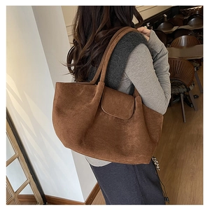 Brown suede tote bag shown on a shoulder in a cozy cafe setting, highlighting large capacity