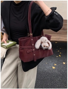 Detalle de bolso tote granate con costuras blancas en contraste y colgante de conejo de peluche