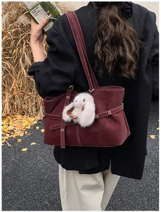 Detail of burgundy suede tote bag featuring a white rabbit fur charm and metal hardware