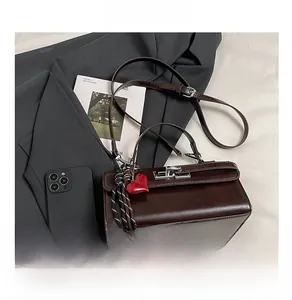 Détail d'un sac en cuir brillant marron foncé avec fermoir argenté et breloque cœur