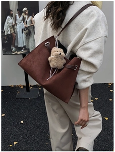 Detail of a brown suede tote bag featuring slim leather straps and a cute plush bear charm
