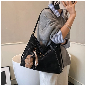 Macro view of black suede tote bag with white contrast stitching and bear charm accessory