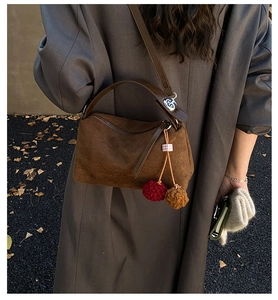 Détail du sac boston en daim marron foncé avec pompon bicolore et poignée en cuir