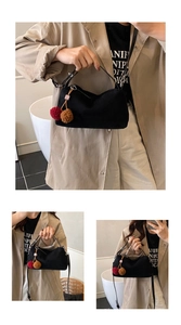 Détail du sac à bandoulière noir mat avec des breloques pompons rouges et marron