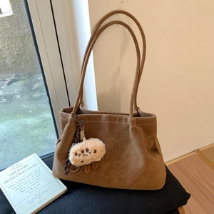 Detail of a brown suede tote bag with slim shoulder straps and a plush cartoon pendant