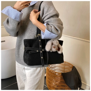 Detail of black suede tote bag with white stitching and plush bunny charm accessory