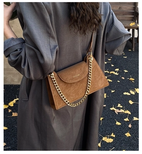 Detail of a brown suede trapezoid bag with gold chain and strap on a winter coat