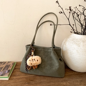 Detail of dark green frosted tote bag with white stitching and plush doll charm