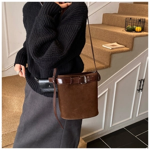 Détail du sac seau en daim avec garniture en cuir et boucle porté par un mannequin