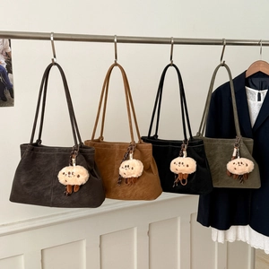 Detail view of four colorful suede tote bags with cute plush charms hanging on a rack