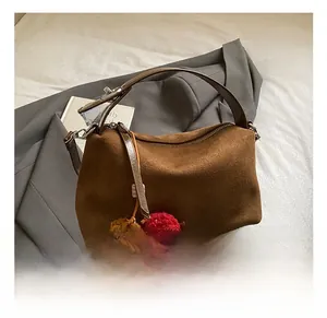 Détail du sac polochon en daim marron avec pompons décoratifs et anses souples