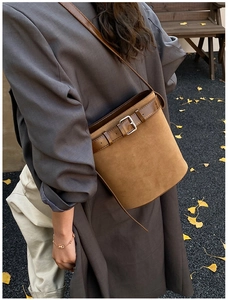 Detail of brown suede bucket bag with buckle strap on a model in autumn scenery